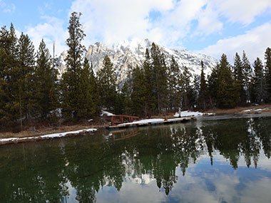 Trees reflect over lake with mountain beyond