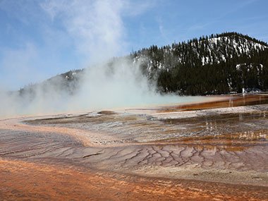 Red pool with steam rising in front of mountain