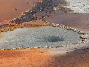Clear pool surrounded by red sediment - Yellowstone National Park