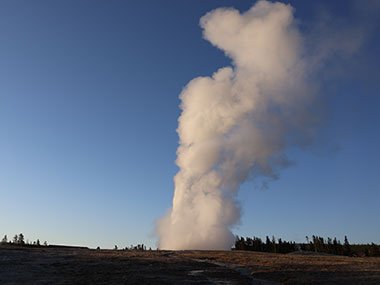 Steam over Old Faithful in front of blue sky