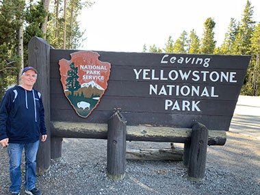 Pat in front of sign leaving Yellowstone National Park
