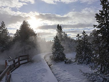 Yellowstone National Park trail covered in snow as sun peeks through clouds