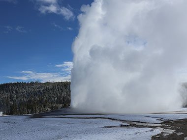 Yellowstone National Park Old Faithful erupts with blue sky in background