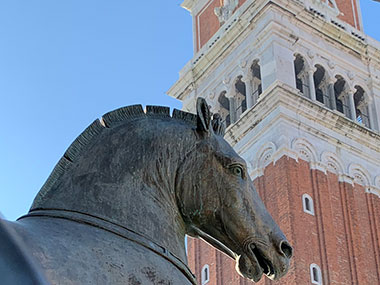 Closeup of horse statue with bell tower behind it