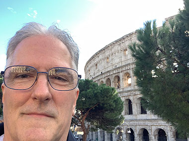 Pat in front of the Colosseum beyond two trees