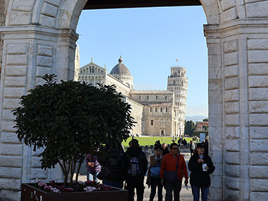 People walking under an arch past a bush