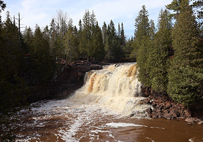 Trees line river next to waterfall