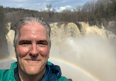 Pat at Grand Portage State Park in front of rainbow and waterfall