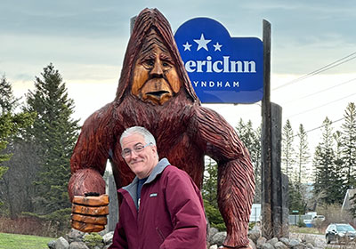 Pat smiles in front of bigfoot statue