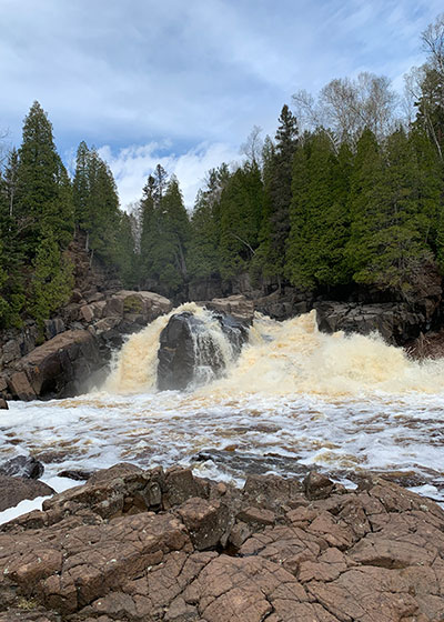 Trees behind waterfall with blue sky