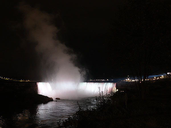 White light shines on Niagara Falls as viewed from Canadian side with mist in the air