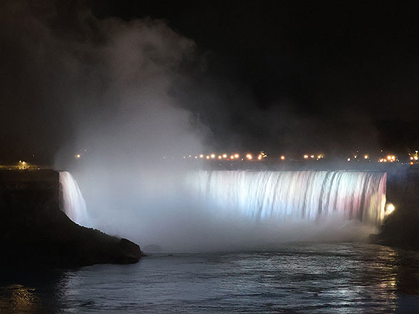 White light shines on Niagara Falls as viewed from Canadian side with mist rising in the foreground