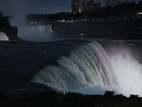 Close up of water flowing over Niagara Falls on American side with other waterfalls in distance at night