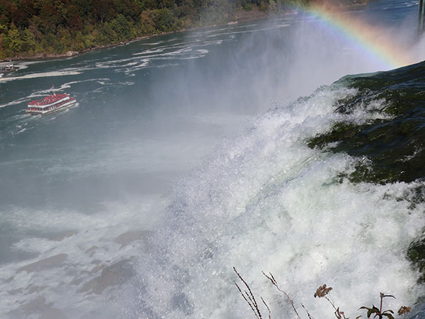 Water flows over Niagara Falls with rainbow in the background