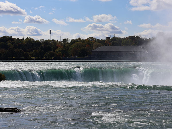 Water flows over the side of Niagara Falls from a distant perspective