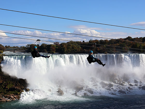 Two people zip line  in front of Niagara Falls as viewed from Canadian side