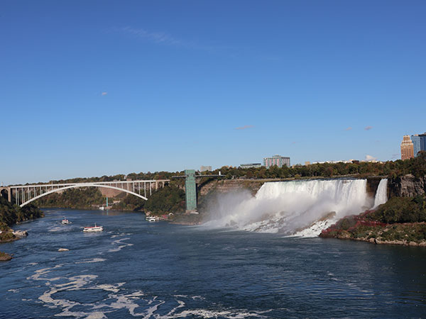 Water flowing over Niagara Falls from Canadian side with bridge in distance